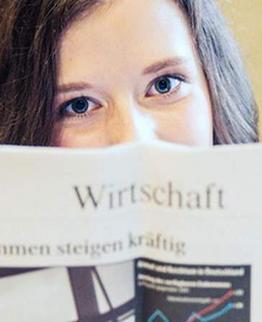 Person hält eine geöffnete Zeitschrift mit Diagramm und deutschem Text.