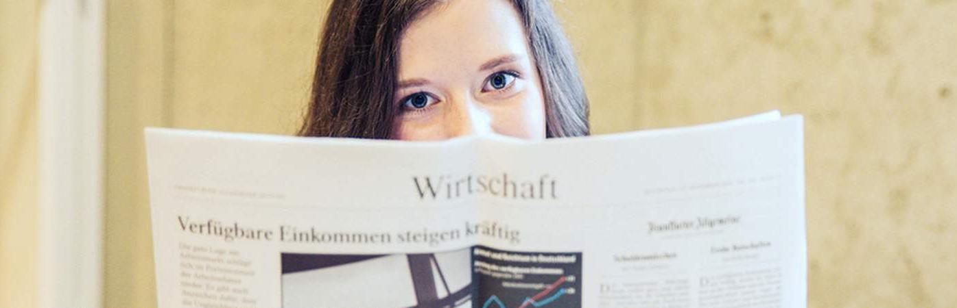 Person hält eine geöffnete Zeitschrift mit Diagramm und deutschem Text.