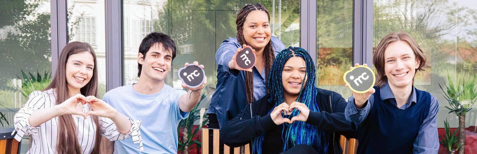 Group of five people sitting side by side making hand gestures for love and peace