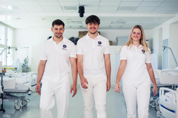 Three IMC students from the medical faculty, dressed in white, walk side by side through one of the IMC Health Labs. All three are laughing into the camera.
