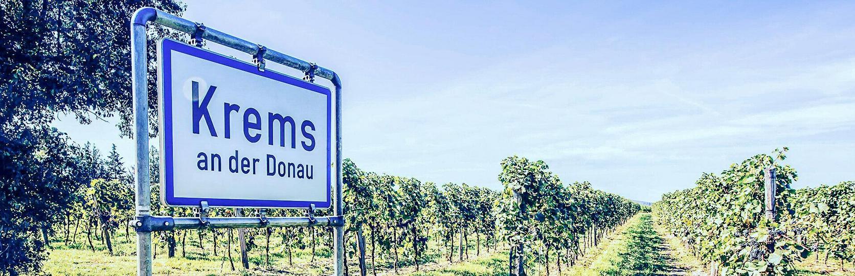 Verkehrsschild Krems an der Donau vor Weinbergen unter klarem Himmel.