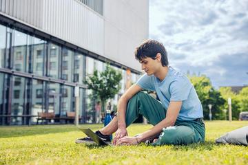 Ein Student sitzt in der Wiese vor dem IMC Krems