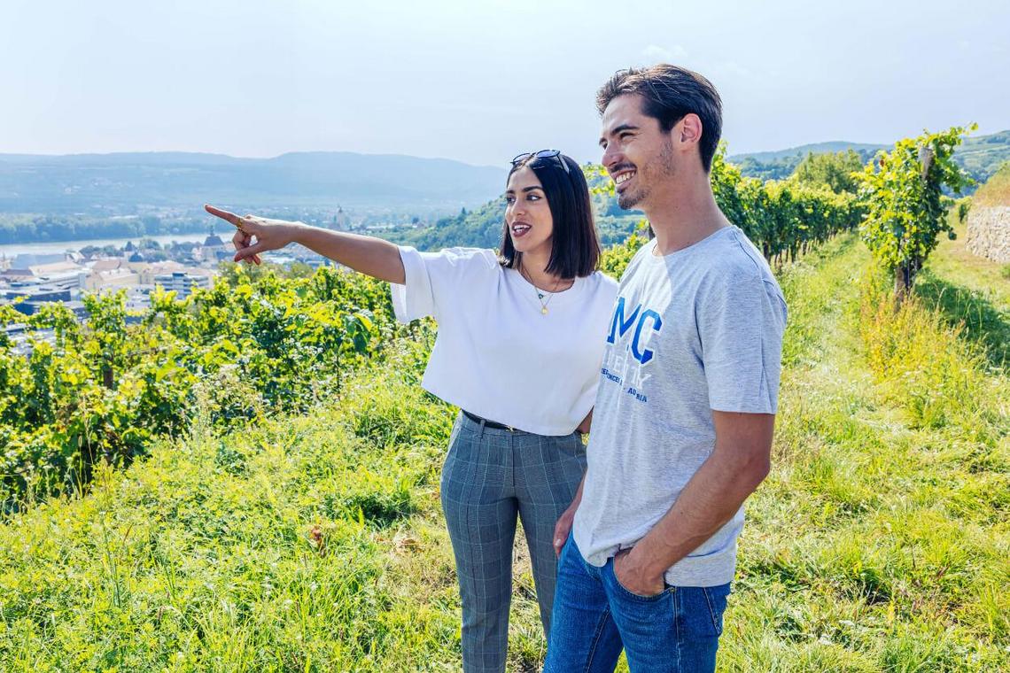2 students stand in the vineyard and point their fingers to the other side