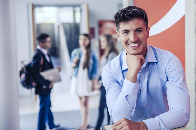 Personen im Flur unserer Hochschule, mit einem nachdenklichen Menschen im Vordergrund und anderen Personen im Hintergrund.