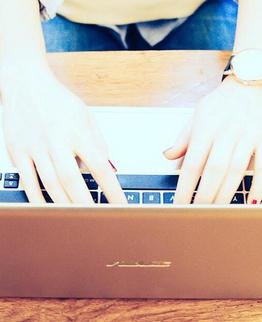 Drei Personen arbeiten an Laptops auf einem Holztisch, Fokus auf den Händen und Tastaturen.