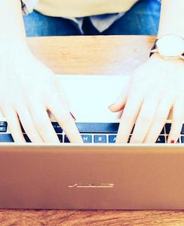 Three individuals working on laptops placed on a wooden table, focus on hands and keyboards.