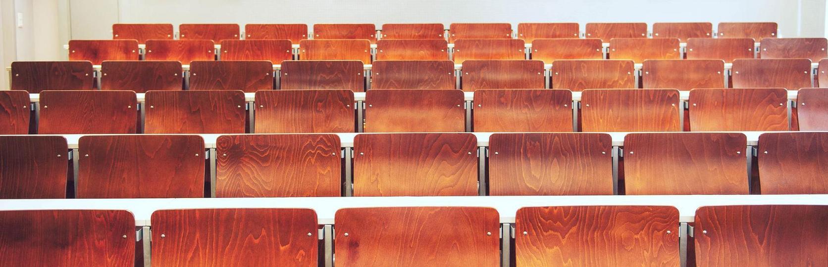Reihen leerer, hölzerner Hörsaalstühle in einem leeren Klassenzimmer.