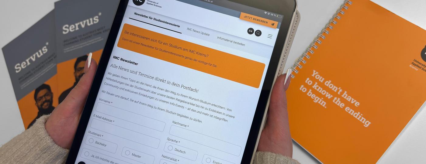 Person hält ein Tablet mit einer geöffneten E-Mail-Anwendung, im Hintergrund unscharfe Broschüren