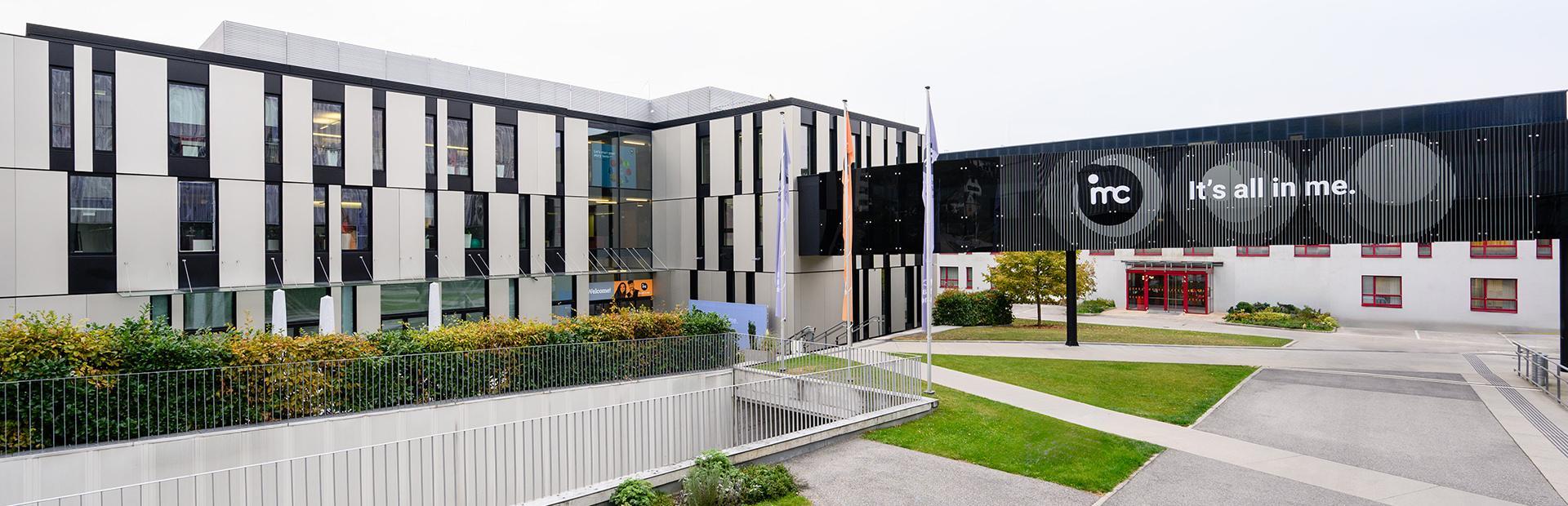 Front view of building G1 at the IMC Campus Krems. The bridge between buildings G & G1 with the large IMC logo and the inscription ‘IMC. It's all in me’ can be seen on the right of the picture.