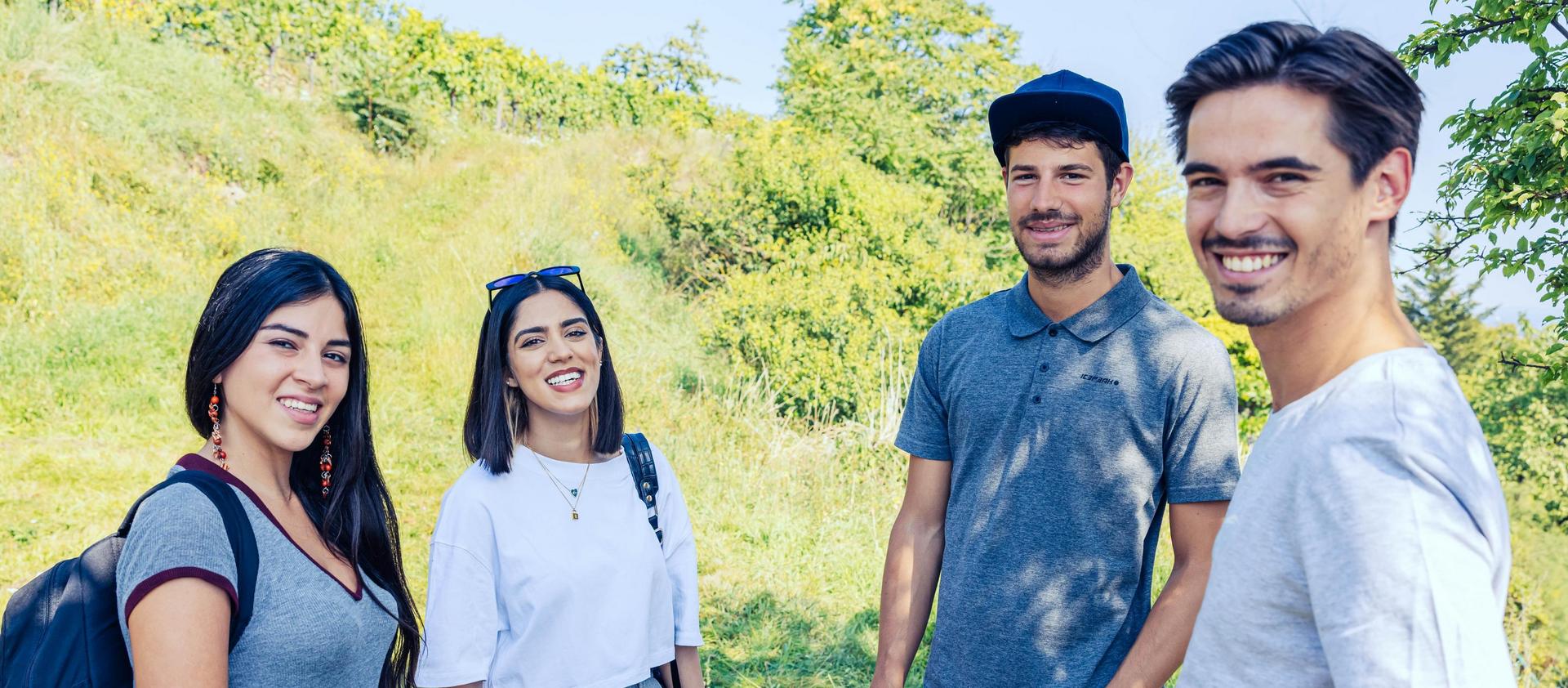 Four individuals with backpacks standing on a path amidst greenery.