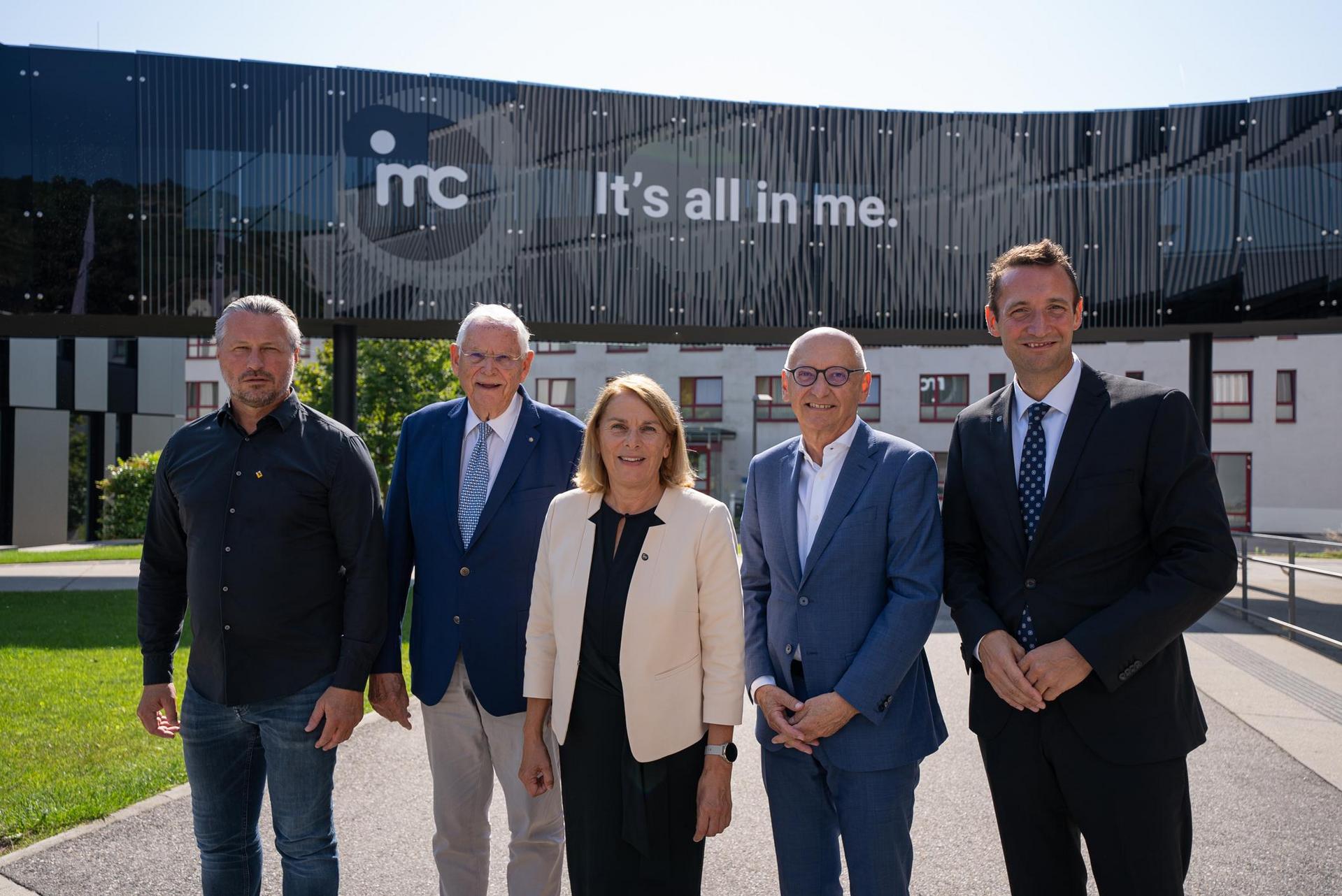 Gruppe von fünf Personen vor einem modernen Gebäude mit der Aufschrift “IMC - It’s all in me.”