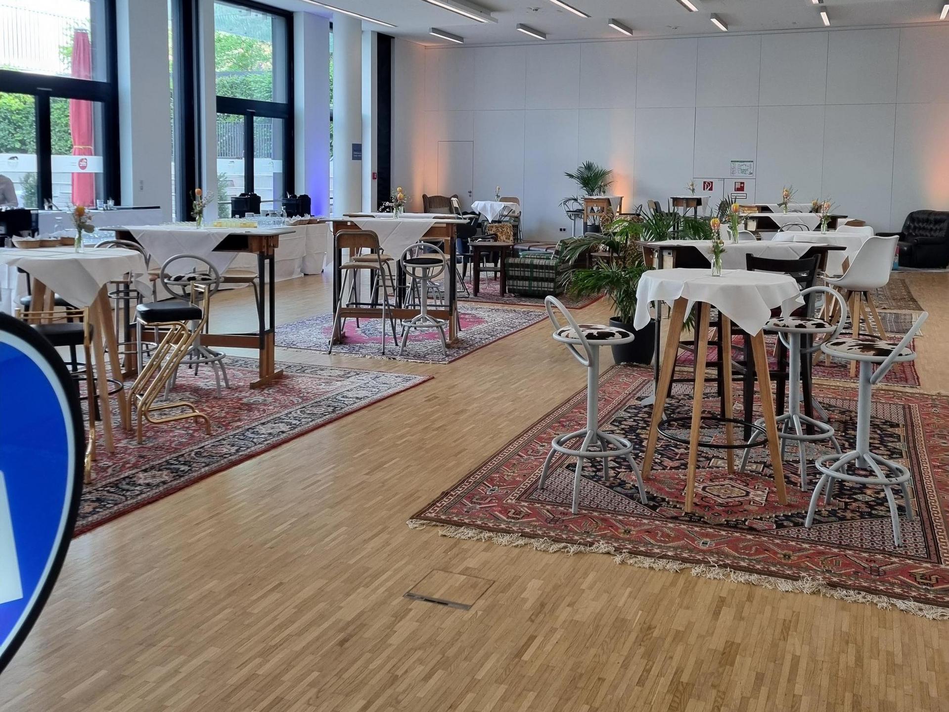 Modernly designed interior with tables and chairs, large windows and plants, illuminated by ceiling lights.