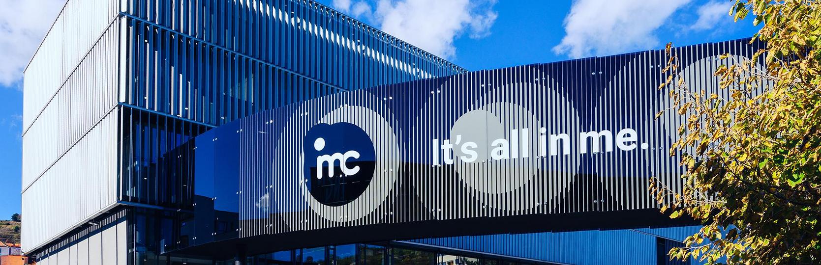 Modern building with blue facade featuring theIMC logo and the slogan it’s all in me in daylight.