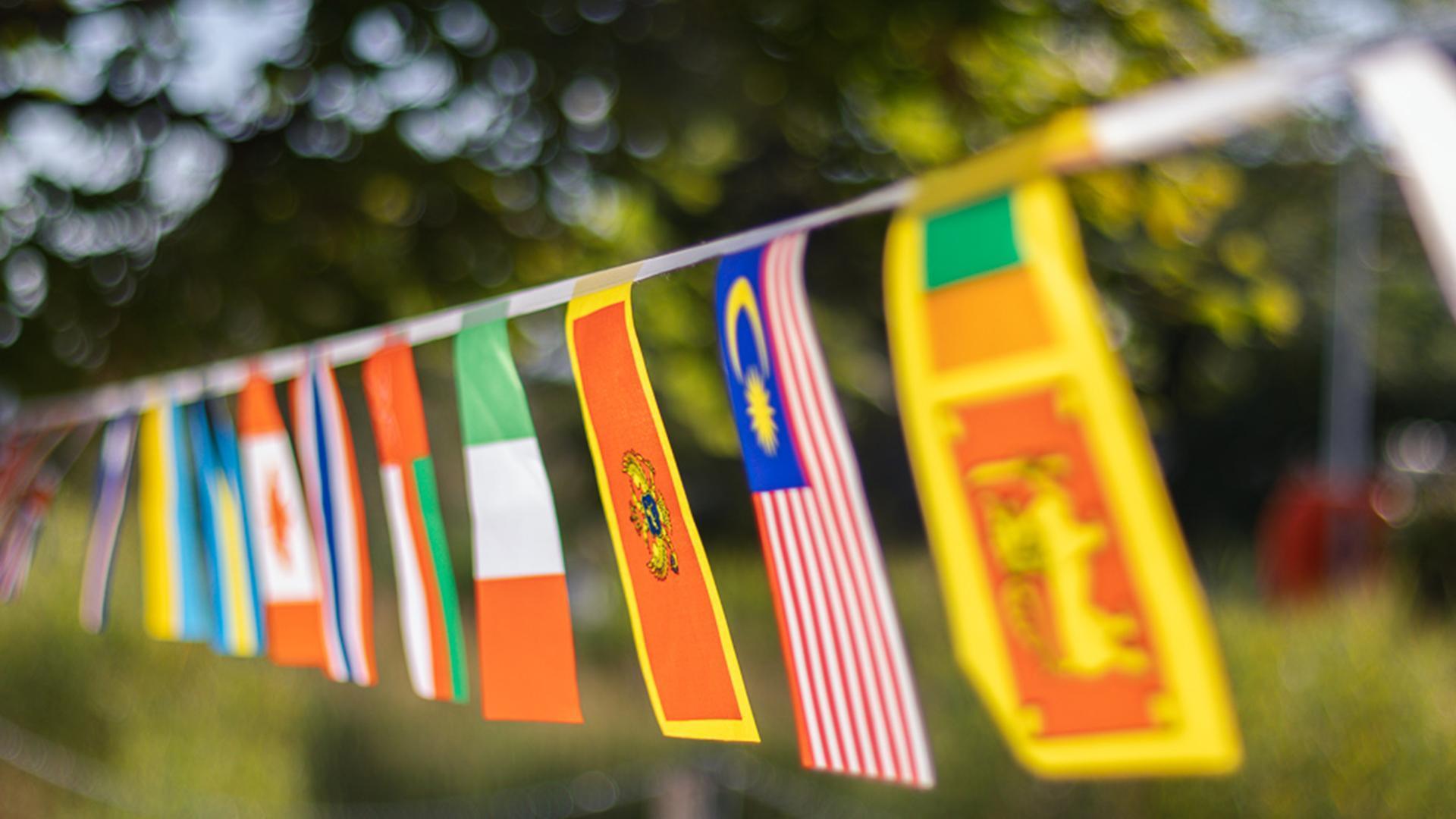 Bunte Fahnen verschiedener Länder an einer Schnur aufgereiht mit unscharfem Hintergrund.