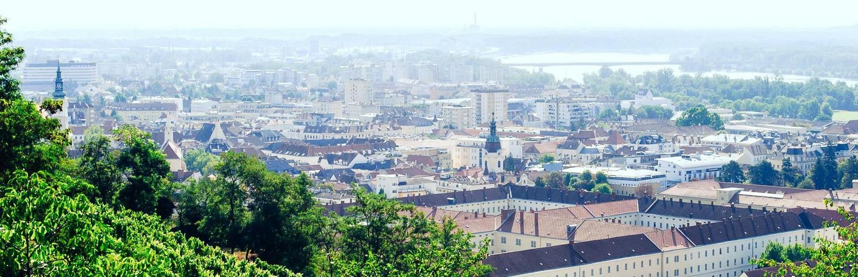 Panoramic view of Krems with buildings and the river danubew in the background, surrounded by trees.