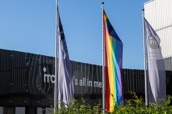 Die IMC Brücke mit drei Flaggen davor, darunter die Pride-Flagge, die für Einheit und Vielfalt steht.