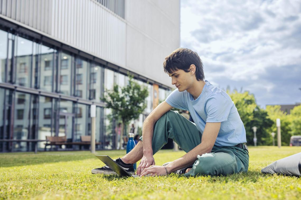 Ein Student sitzt auf einer Wiese