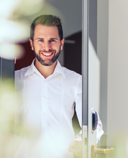 Person in weißem Hemd steht hinter teilweise geöffneter Tür