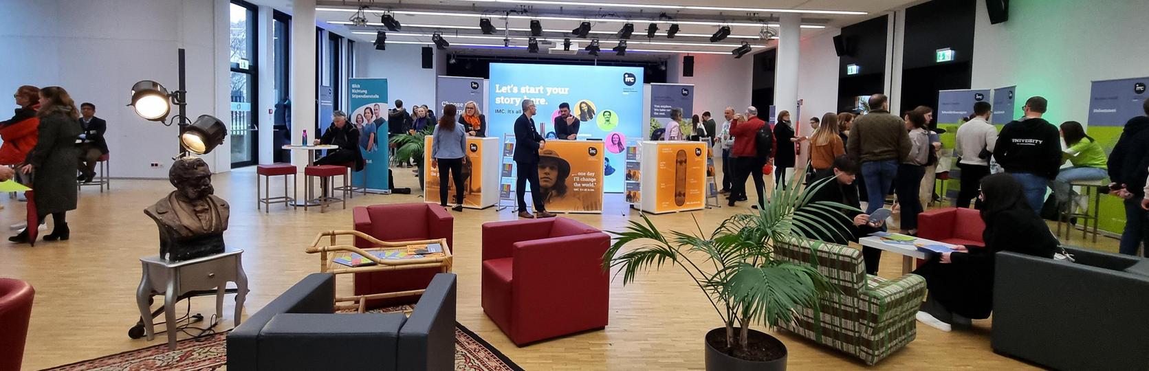 Conference room with people networking and information booths in the background.