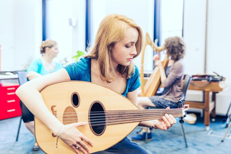 Eine Person spielt ein Oud in einem Musikeinheit an einer österreichischen Hochschule, während im Hintergrund jemand Harfe spielt.