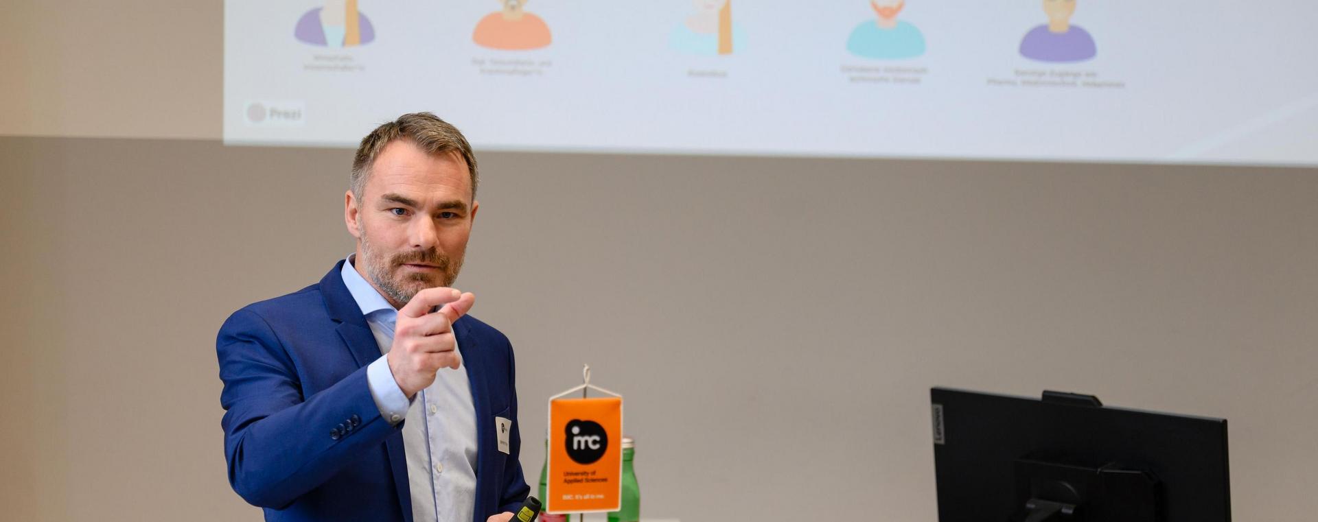 Person standing in front of an audience delivering a presentation in a lecture hall.