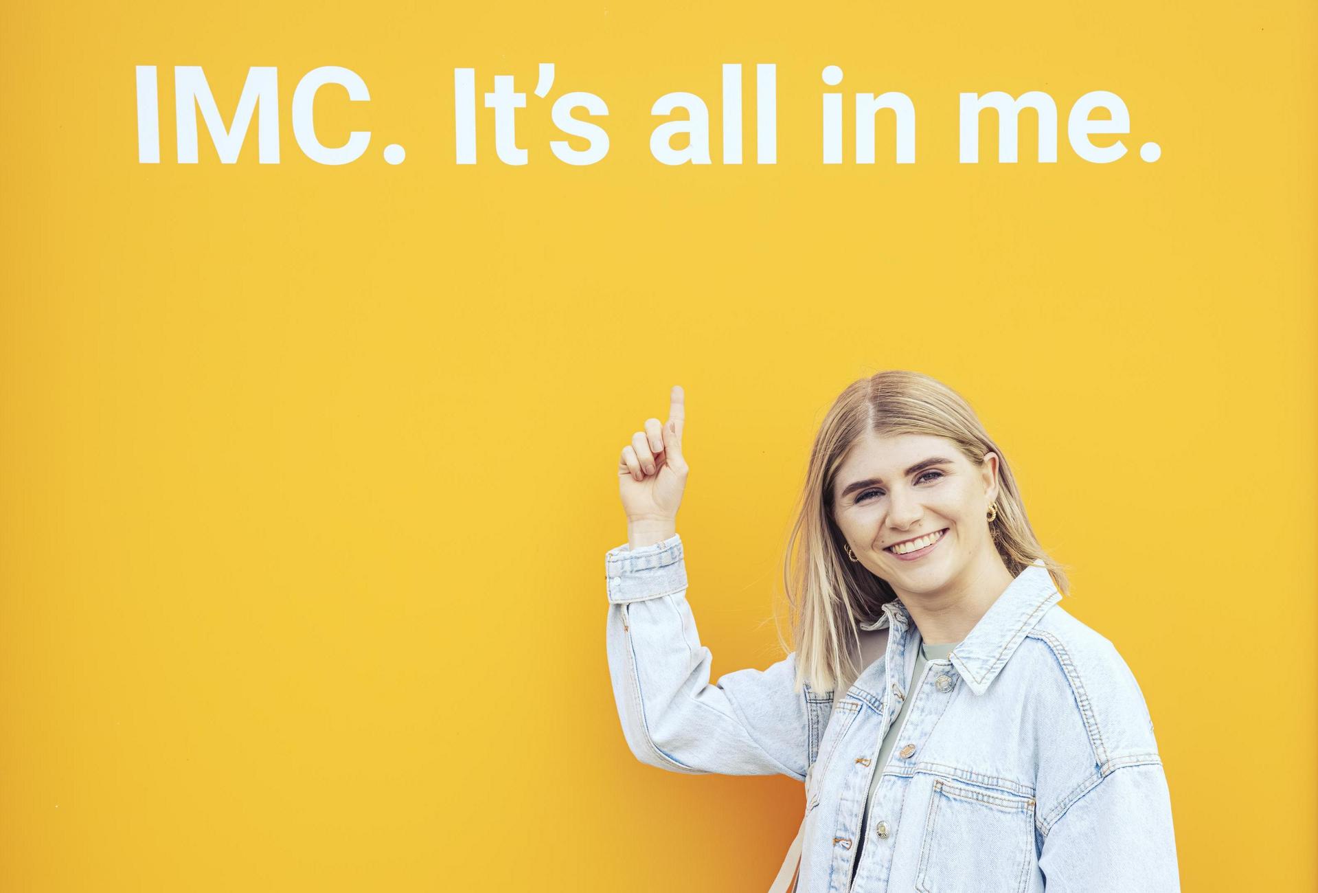 Studentin steht vor einem Plakat mit der Aufschrift "IMC. It's all in me."