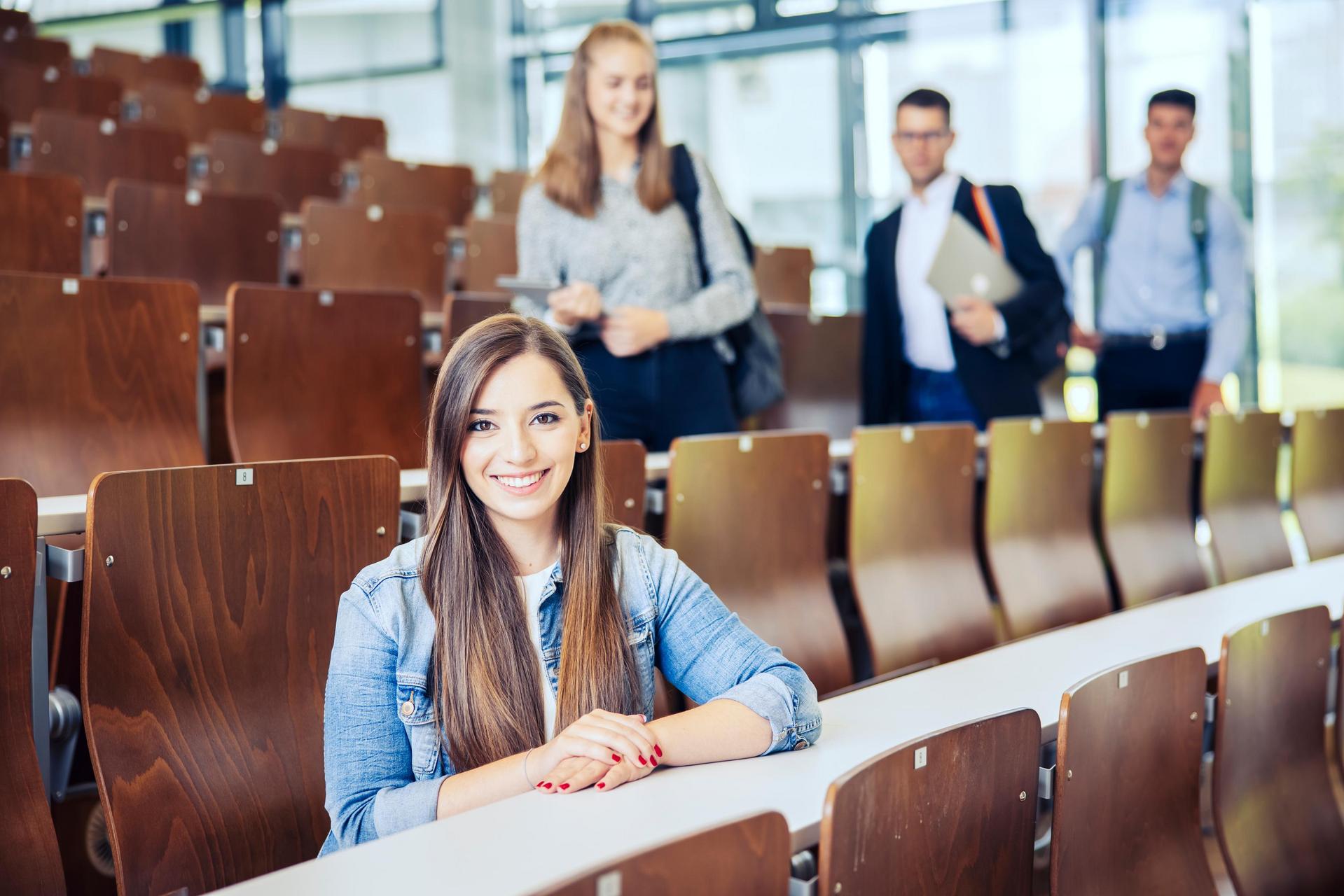 Studenten sitzen und stehen in einem Hörsaal mit Holzstühlen.