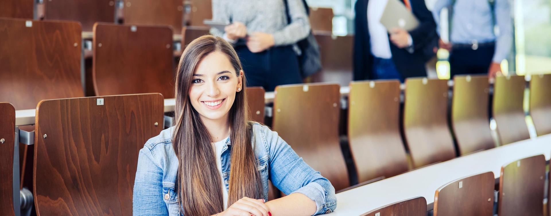Studenten sitzen und stehen in einem Hörsaal mit Holzstühlen.